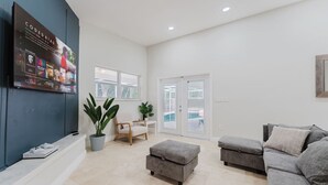 A spacious living area with a grey sofa, a grey ottoman, a wooden chair, and a potted plant. - 5BD Beach House, Sun, Pool, BBQ & Shop! Beach & Aventura Mall – Sleeps 26! (Miami)