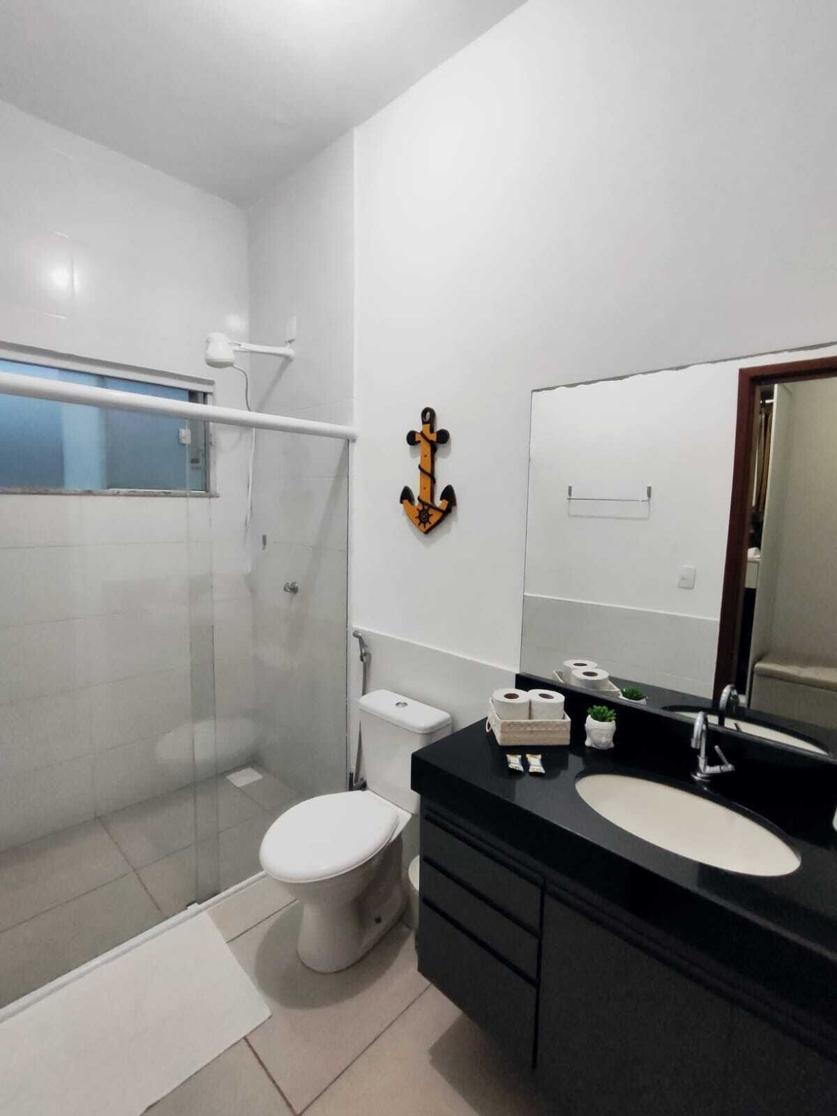 A modern bathroom with a glass shower enclosure, a white toilet, a black vanity with a large mirror, and a small potted plant.