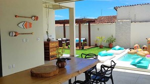 A patio area with a wooden table and chairs, a small pool with inflatable toys, and a view of the backyard.