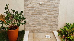 A stone wall with a built-in shower, a potted plant, and a small drainage grate.