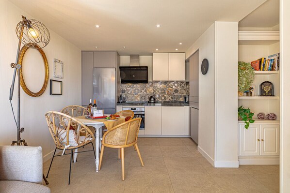 A modern kitchen with white cabinets, a tiled backsplash, and a dining area with wicker chairs.