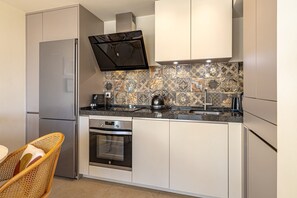 Cozinha compacta com forno embutido, cafeteira e chaleira sobre a bancada.