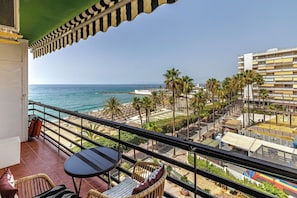 Uma varanda com vista para o mar, palmeiras e um prédio com varandas.