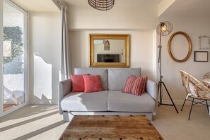 A modern living room with a grey sofa, red and patterned cushions, a wooden coffee table, a floor lamp, and a large mirror on the wall.