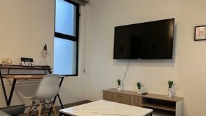 A modern living room with a flat-screen TV mounted on the wall, a wooden desk with a chair, and a sofa. - Cozy 2-bedroom condo with rooftop terrace w/arch view in Cabo San Lucas (cabo san lucas)
