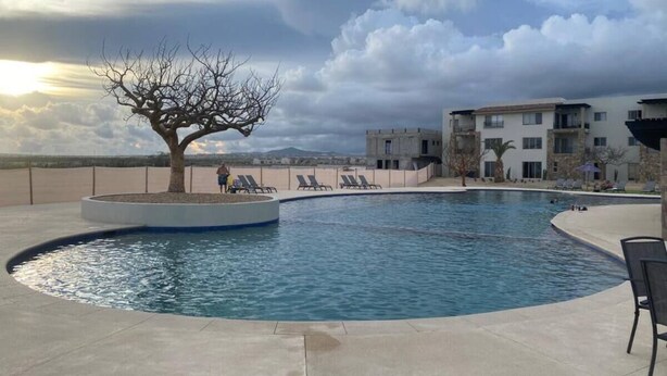 A swimming pool with lounge chairs, a tree, and a building in the background. - Cozy 2-bedroom condo with rooftop terrace w/arch view in Cabo San Lucas (cabo san lucas)