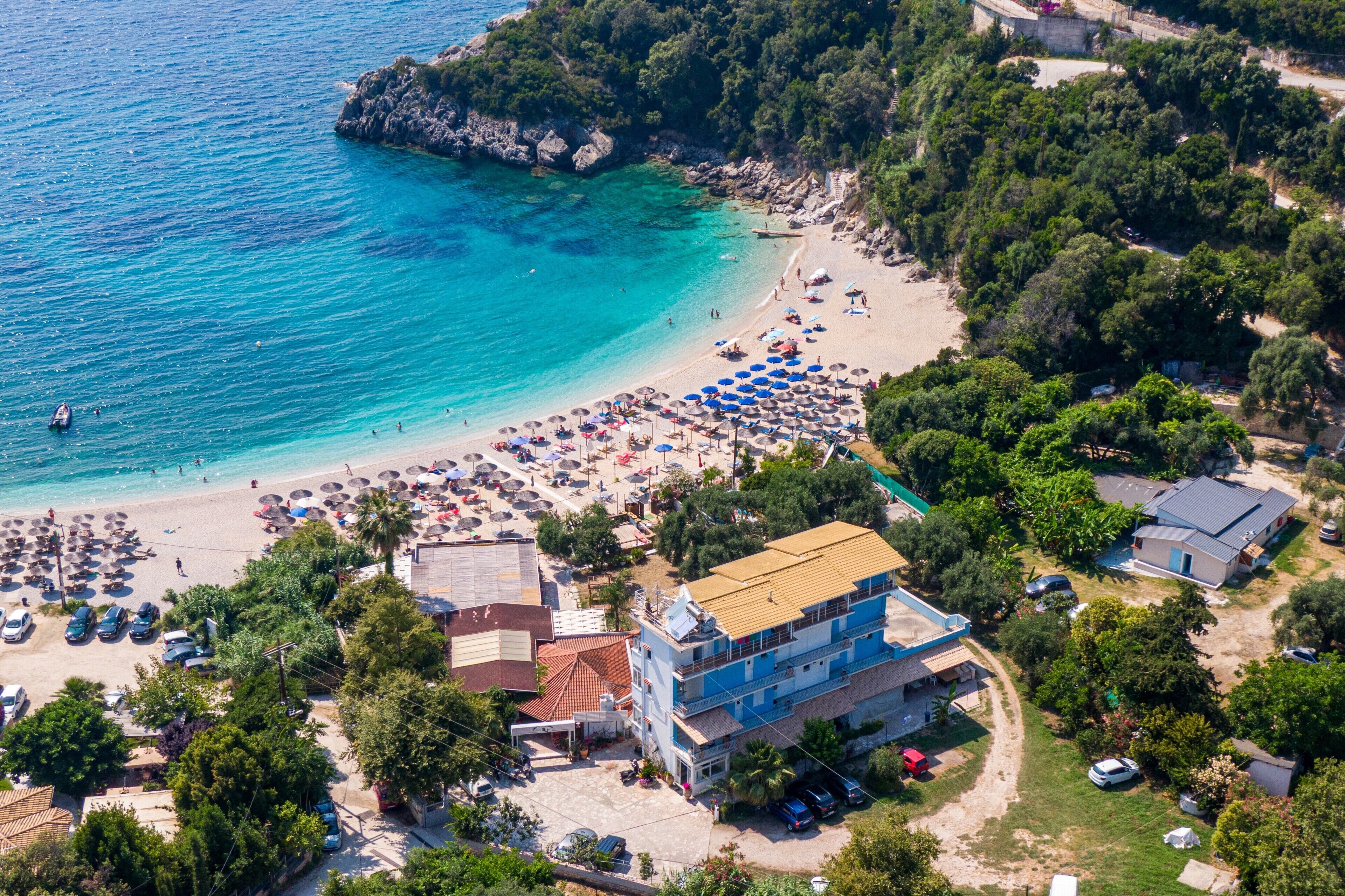 An aerial view of a coastal area with a beach, umbrellas, and buildings.