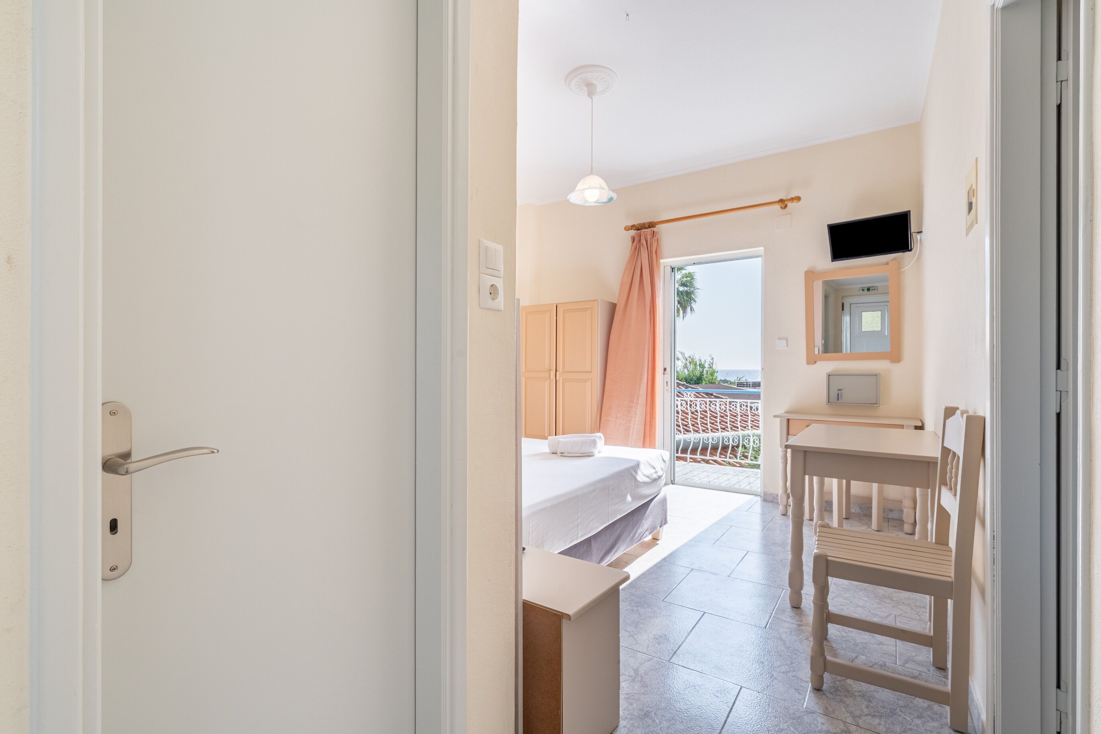Et værelse med seng, skrivebord, stol, fjernsyn og en balkon med udsigt.