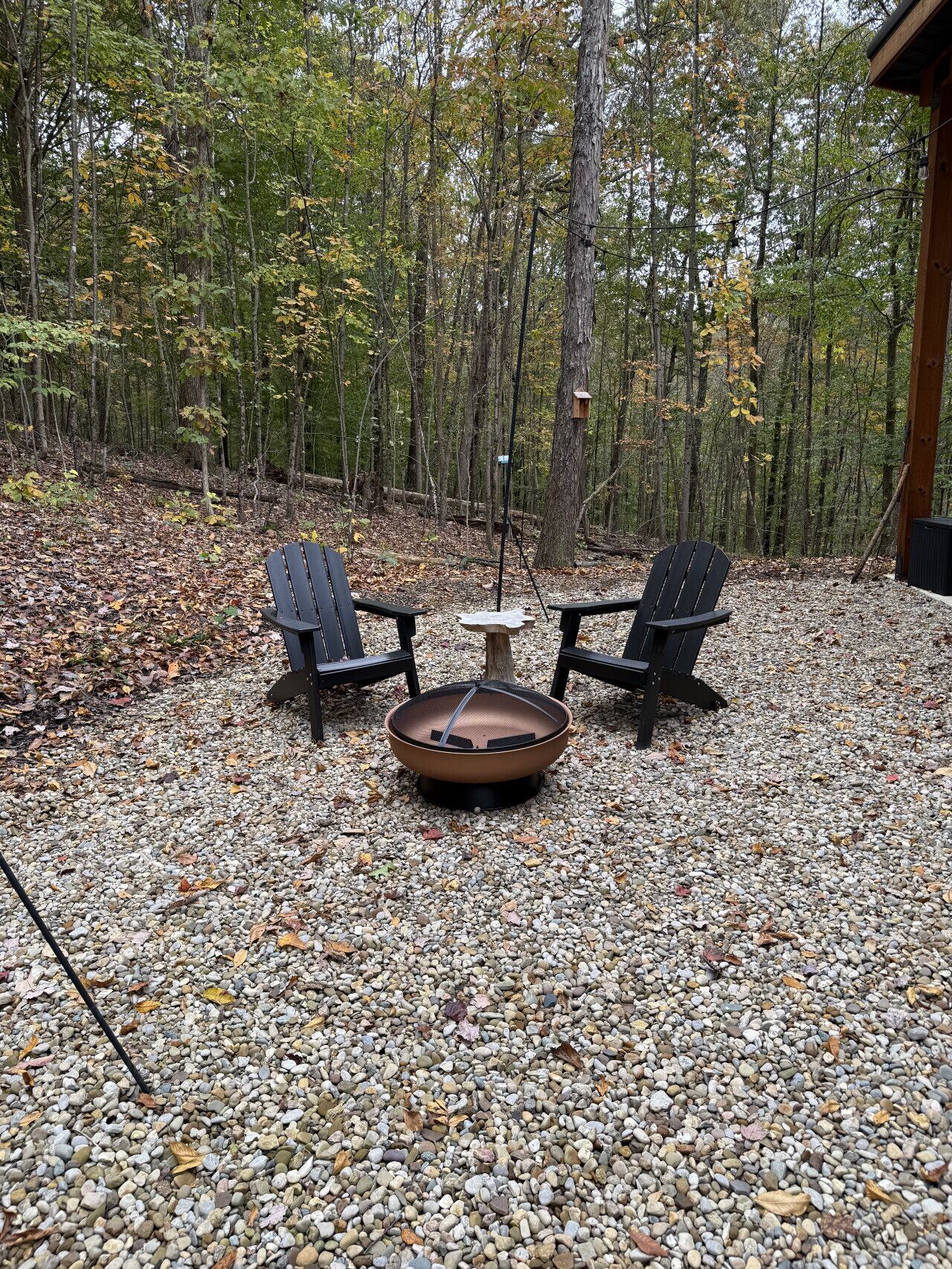 Un área de estar al aire libre con dos sillas Adirondack y un brasero rodeado de piedras y árboles.
