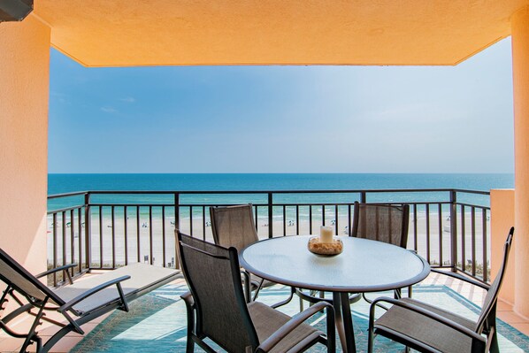 Een balkon met een tafel en stoelen, met uitzicht op een strand en de oceaan.