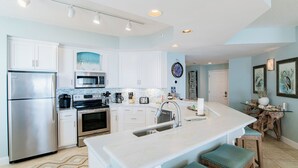 A modern kitchen with white cabinets, stainless steel appliances, and a central island with stools. - Sea Chase Resort, Gulf Front Condo 3 bd/3 ba, Fitness Room, 5 pools, 4 Hot Tubs (Orange Beach)
