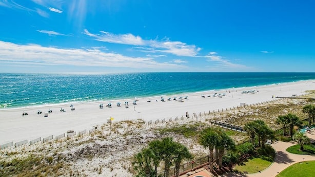 A beach with a clear sky, sandy shore, and a few umbrellas. - Sea Chase Resort, Gulf Front Condo 3 bd/3 ba, Fitness Room, 5 pools, 4 Hot Tubs (Orange Beach)