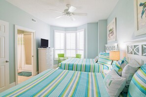 Ein Schlafzimmer mit zwei Betten, einem Deckenventilator, einem Fernseher, einem Sessel und einem Fenster mit Rollläden.