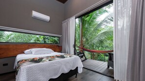 Een slaapkamer met een bed, een raam met uitzicht op groen, een hangmat en een airconditioner aan het plafond.