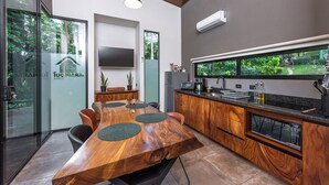Een moderne keuken met een houten eettafel, inbouwapparatuur en een groot raam met uitzicht op groen.