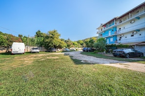 A residential area with a paved driveway, parked cars, and a multi-story building with balconies.