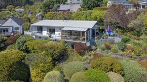 A modern house with a large glass extension, surrounded by lush gardens and other residential buildings.