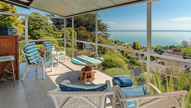 A balcony with wicker furniture, a small table, and a view of the sea.