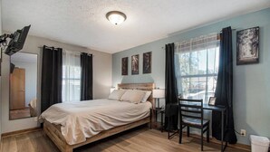 A bedroom with a wooden bed, a desk, a chair, a lamp, and a window with curtains. - Modern 4BR Gretna NE, Garage, Fenced Yard, W/D, Pet-Friendly, Near Outlets (Gretna)