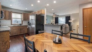 A modern kitchen with wooden cabinets, a stainless steel refrigerator, and a dining area with a wooden table and chairs. - Modern 4BR Gretna NE, Garage, Fenced Yard, W/D, Pet-Friendly, Near Outlets (Gretna)
