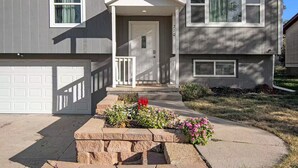 A two-story house with a front porch, a garage, and a well-maintained flower bed. - Modern 4BR Gretna NE, Garage, Fenced Yard, W/D, Pet-Friendly, Near Outlets (Gretna)