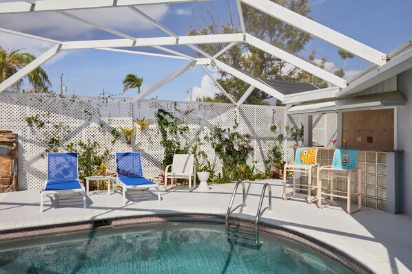 A pool area with a covered section, lounge chairs, and a small table. - Waterfront home near beaches, Multi month discount - inquire (Fort Myers)