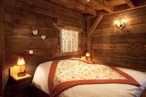 Una habitación tipo cabaña de madera con una cama, dos lámparas de noche, una ventana con cortinas y una lámpara fijada a la pared.