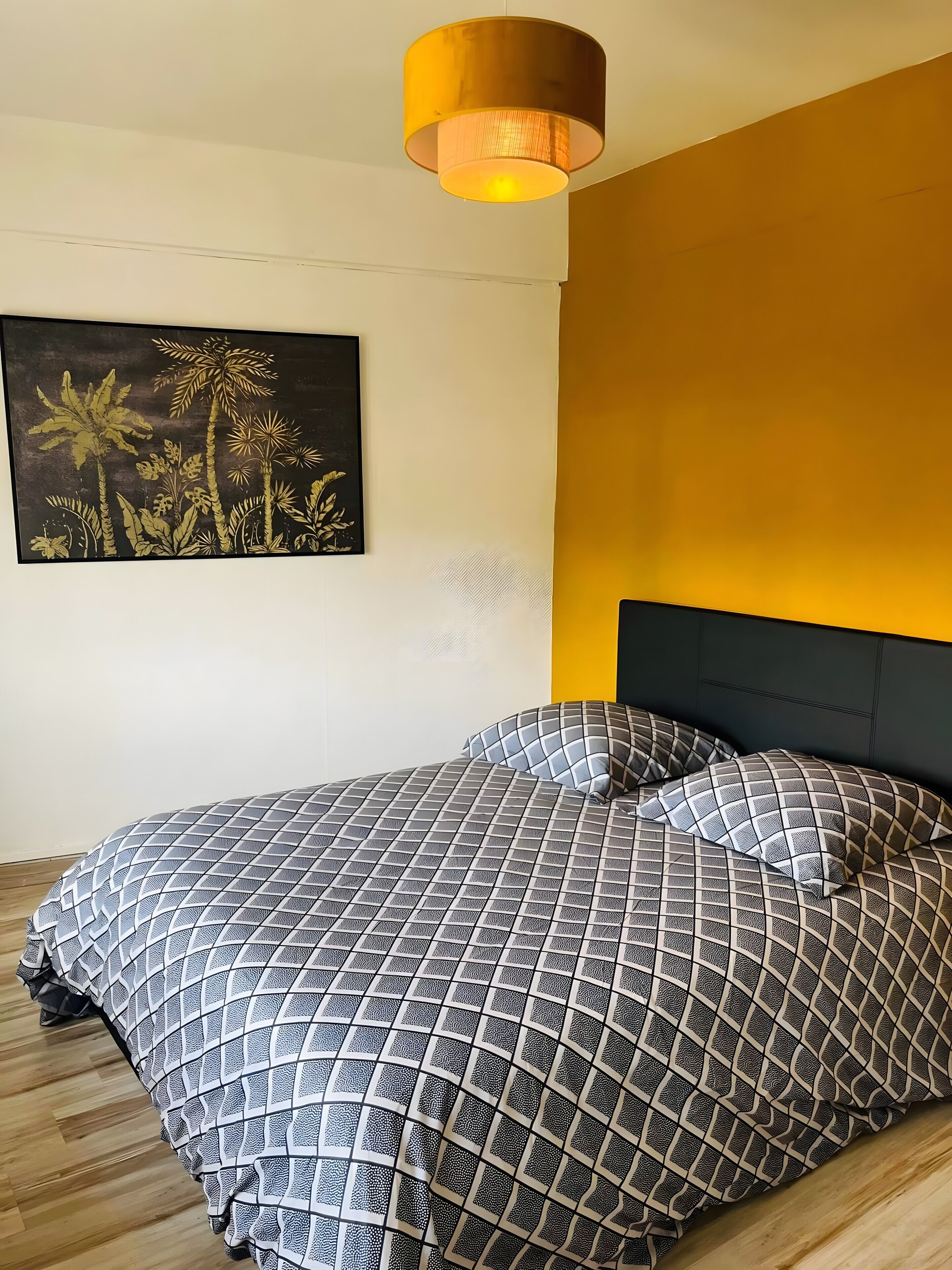 A bedroom with a bed, a headboard, a wall-mounted artwork, and a ceiling light fixture.