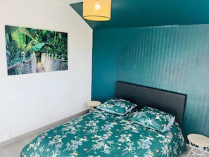 Un dormitorio con una cama, un cuadro en la pared, una lámpara en el techo y un papel tapiz estampado.