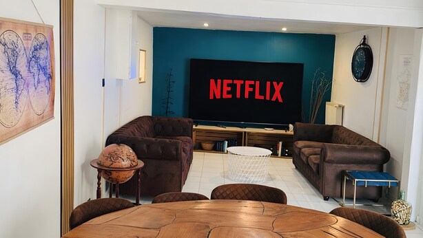 A modern living room with a round wooden table, brown leather sofas, a large flat-screen TV, and a decorative globe. - Gîte Le Flot House with Private Garden and Wi-Fi (Saint-Florentin)