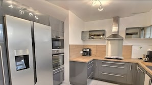 A modern kitchen with a stainless steel refrigerator, built-in oven, and a coffee maker on the counter. - Gîte Le Flot House with Private Garden and Wi-Fi (Saint-Florentin)
