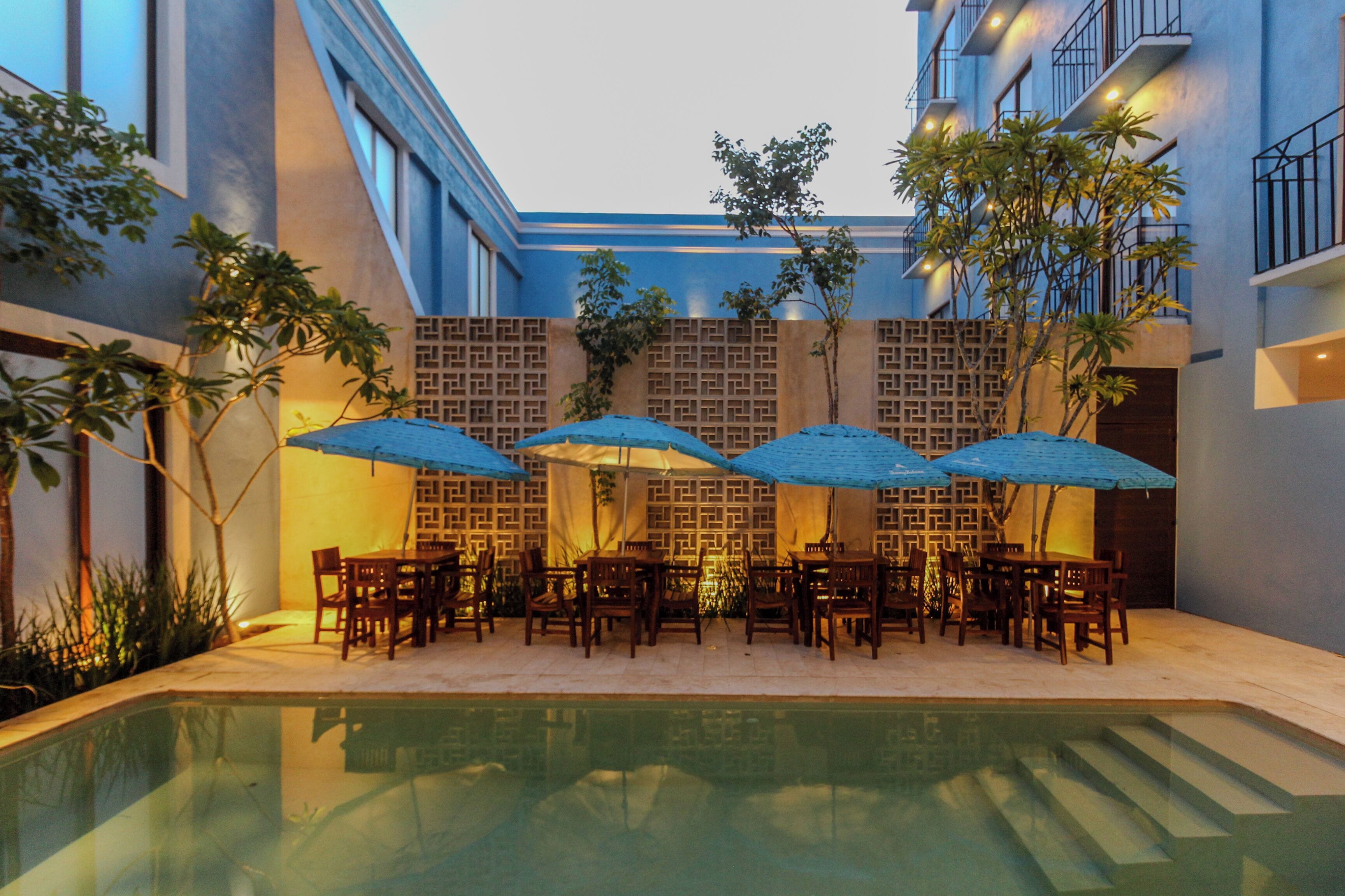 Zona de piscina con mesas, sillas, sombrillas y una pileta.