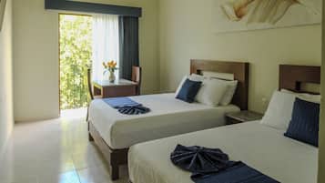 Habitación de hotel con dos camas, una mesita con un florero y vistas a la vegetación a través de una puerta.