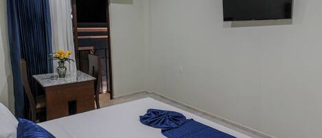 A hotel room with two beds, a small table with a vase of flowers, a TV on the wall, and a balcony with a chair.