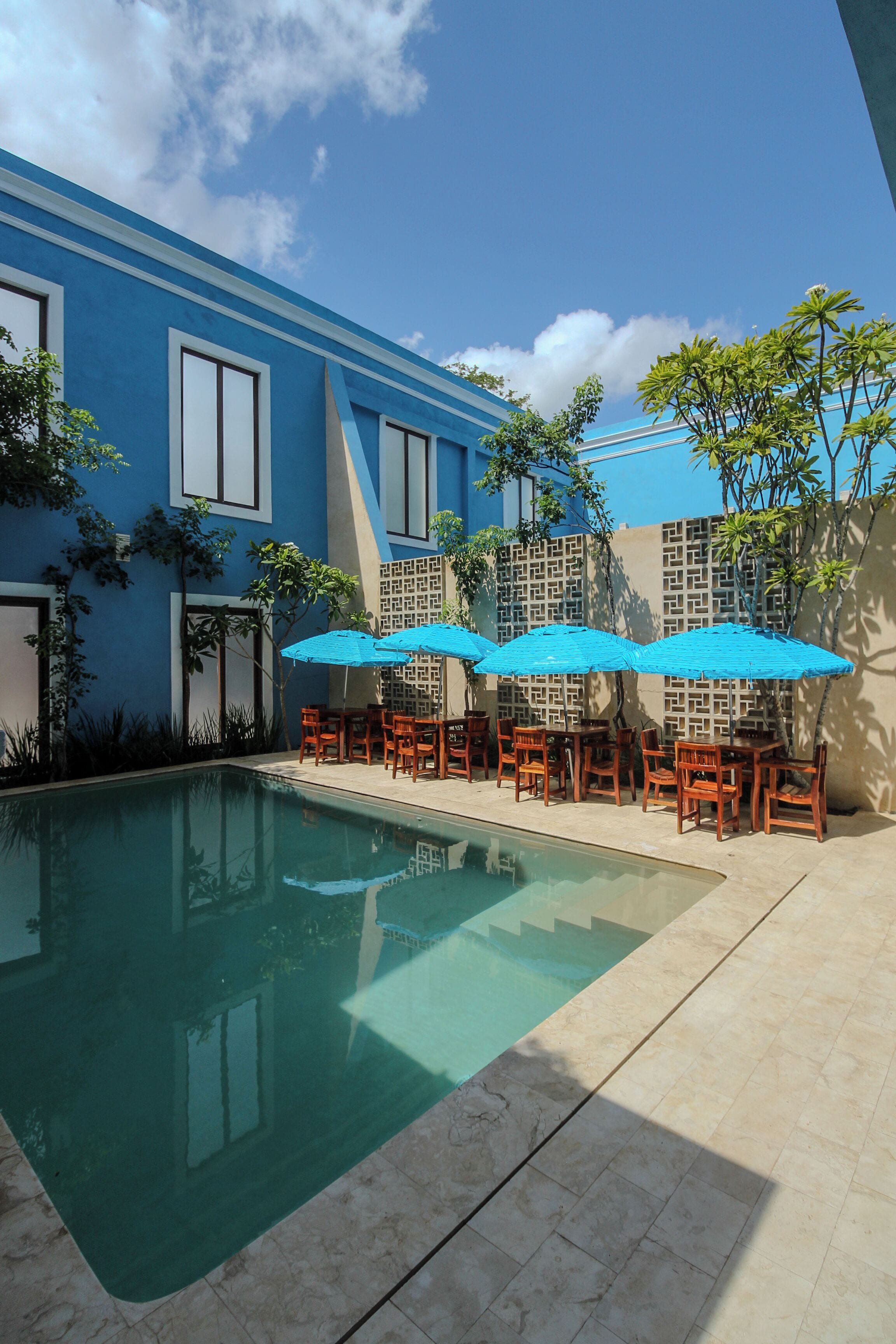 A pool area with blue-tiled flooring, wooden tables and chairs, and blue umbrellas.