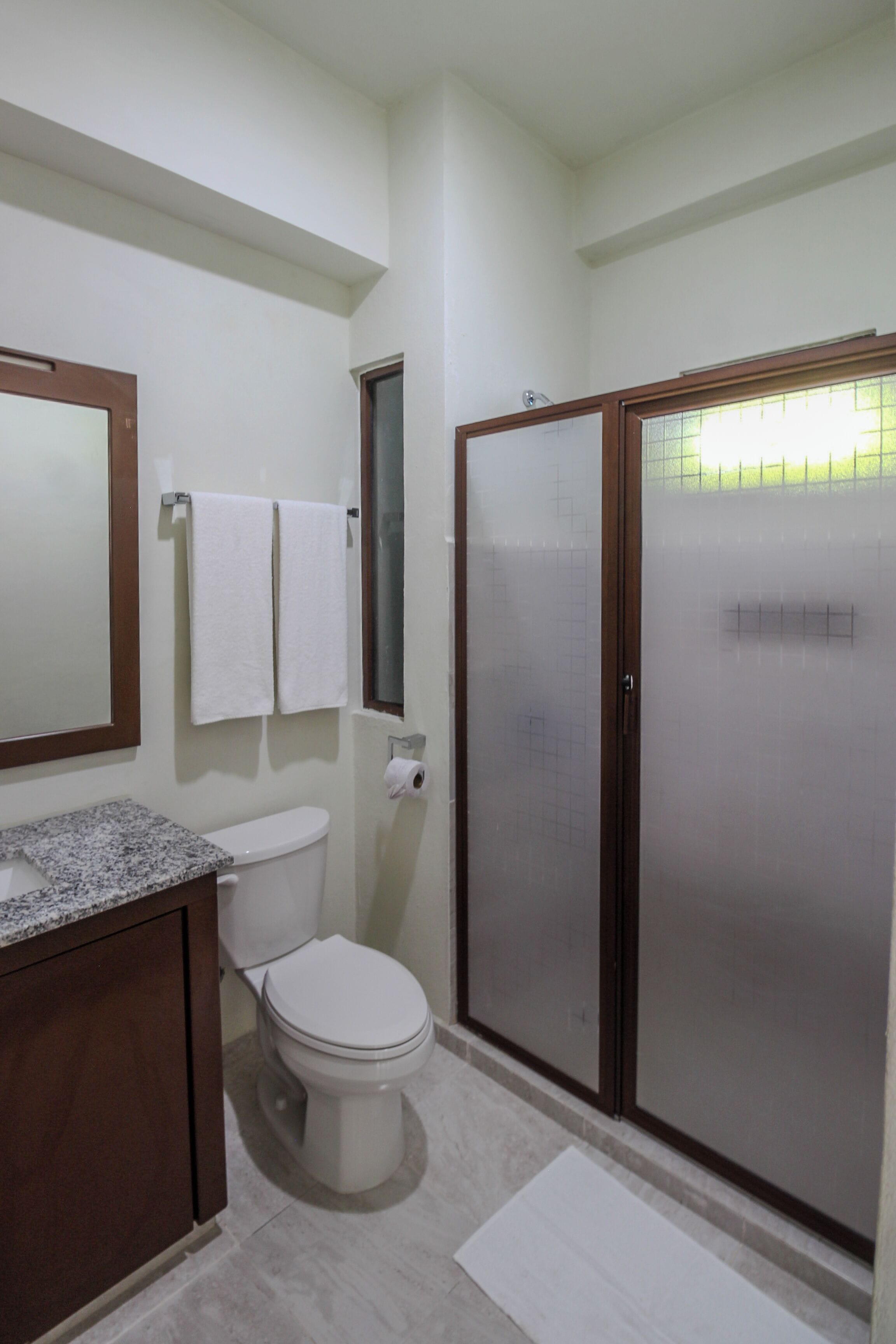 A bathroom with a toilet, a sink, a mirror, and a shower enclosure.