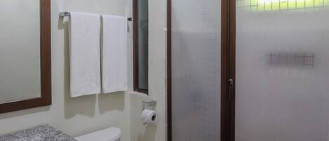 A bathroom with a toilet, a sink, a mirror, and a shower enclosure.