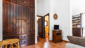 A room with a large wooden wardrobe, a television on a wooden stand, a wicker table, and a cushioned sofa.