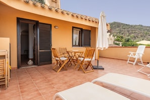 A terrace with a table and chairs, a sun lounger, and a view of a hill.