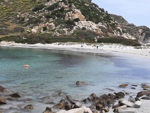 Una playa rocosa con aguas cristalinas, una orilla arenosa y montañas al fondo.