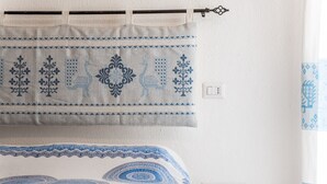A bed with a blue and white patterned bedspread, a small bedside table with a white object, and a wall-mounted curtain with blue patterns.