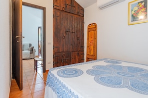 A bedroom with a bed, wooden wardrobe, and a door leading to another room.