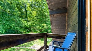 Una terraza de madera con una silla azul, con vista a un área boscosa.