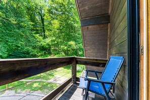 A wooden deck with a blue chair, overlooking a forested area. - The Retreat at Wildcat Hollow (Rockbridge)