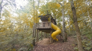 A wooden treehouse with a yellow slide attached to a platform.