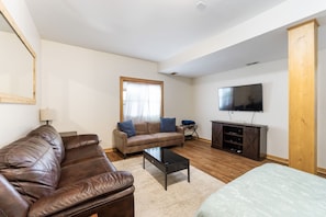 A living room with a brown leather sofa, a beige armchair, a wooden coffee table, and a flat-screen TV mounted on the wall. - The Retreat at Wildcat Hollow (Rockbridge)