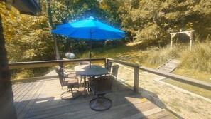 Une terrasse en bois avec une table et des chaises, un parasol bleu et une clôture en métal.