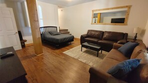 A living room with a brown leather sofa, a gray sofa, a coffee table, a wooden floor, a white door, and a mirror on the wall. - The Retreat at Wildcat Hollow (Rockbridge)