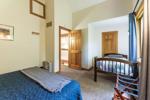 A bedroom with a bed, a chair, a wooden door, and a window with curtains. - The Retreat at Wildcat Hollow (Rockbridge)