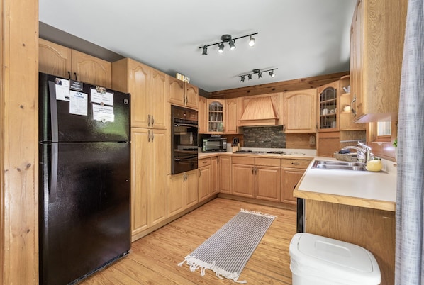 A kitchen with wooden cabinets, a black refrigerator, a microwave, and a sink. - The Retreat at Wildcat Hollow (Rockbridge)
